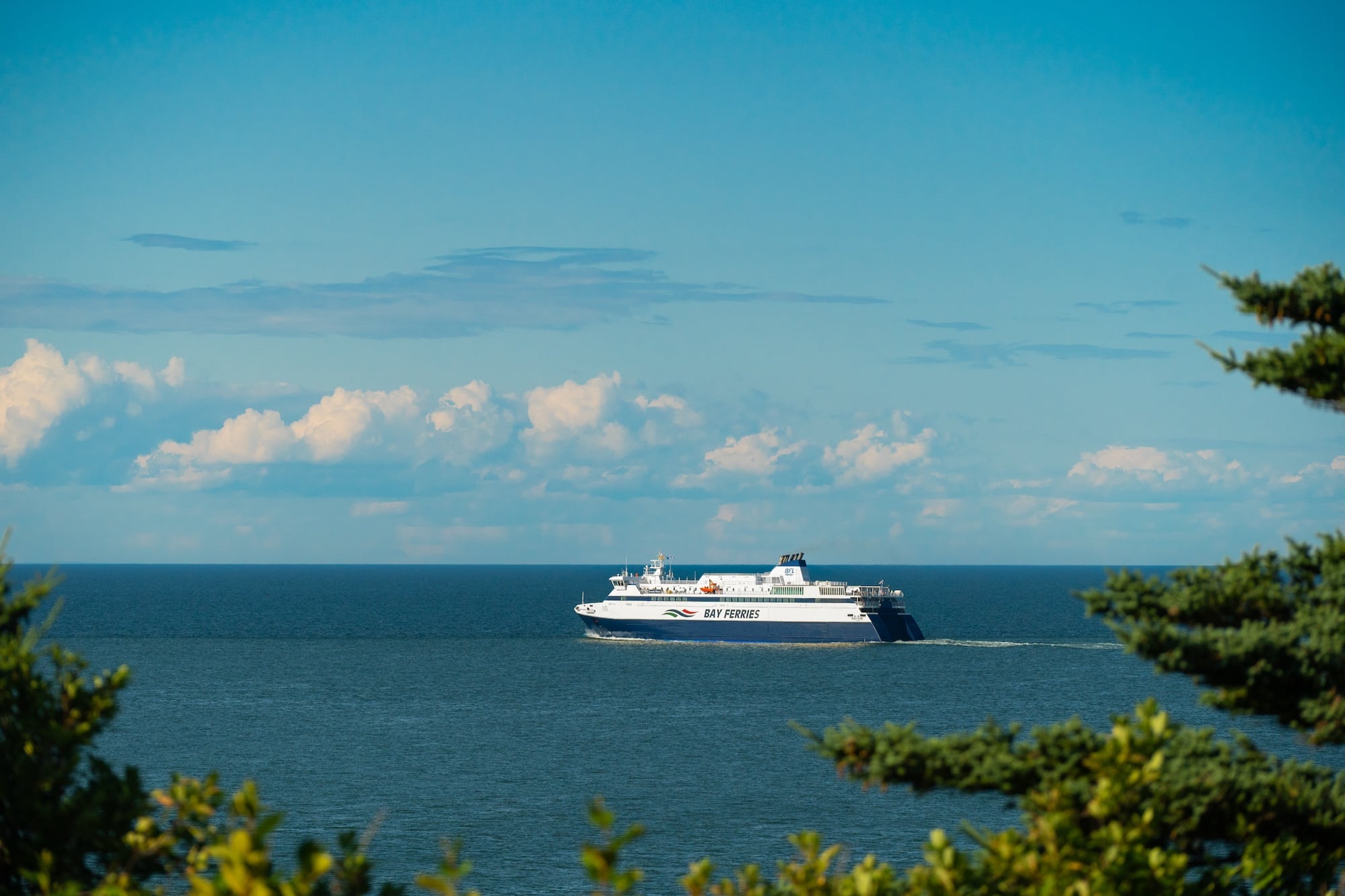A large ferry sailing in the ocean from a distance on a sunny day, blue skies with a few clouds.
